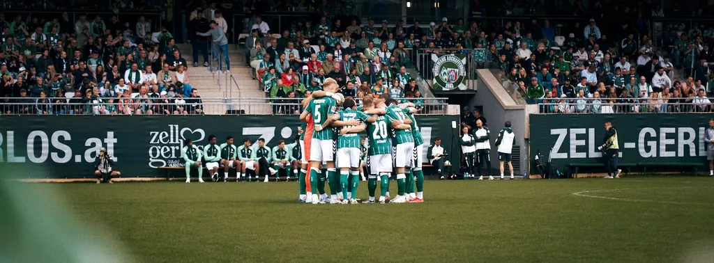 Fußballspiel in Zell am Ziller: Mannschaft in grünen Trikots bildet vor vollen Rängen einen Kreis