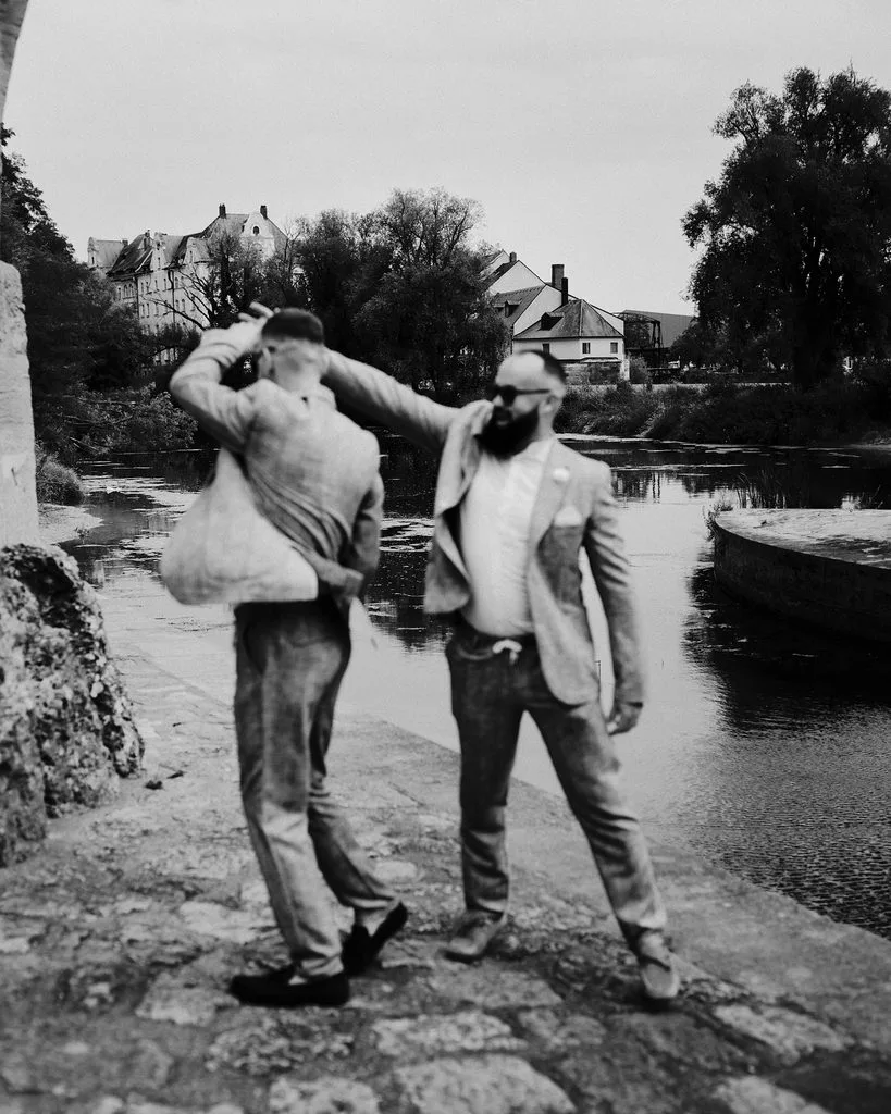 Zwei Bräutigame tanzen ausgelassen am Ufer bei der Steinernen Brücke in Regensburg, Schwarz-Weiß