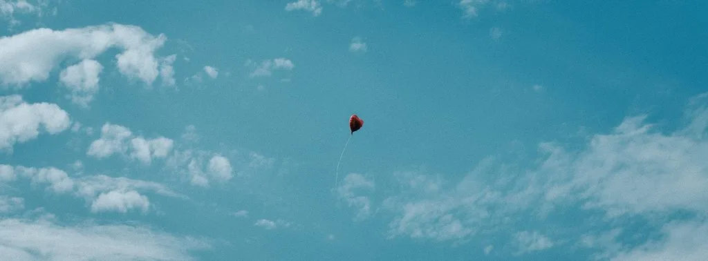 Roter Herzluftballon steigt bei der Hochzeit in den blauen Himmel