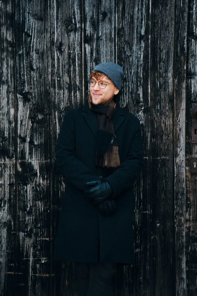 Marcel Schultze, Hochzeitsfotograf aus Niederbayern, im Wintermantel vor einer alten Holztür