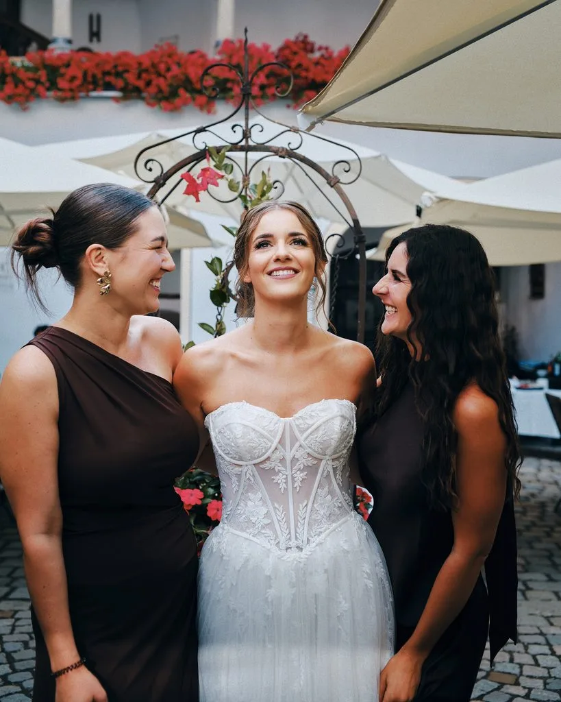 Braut im Corsagenkleid lacht mit zwei Freundinnen im Innenhof