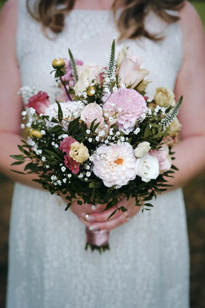 Braut hält einen bunten Brautstrauß mit Rosen, Pfingstrosen und Schleierkraut