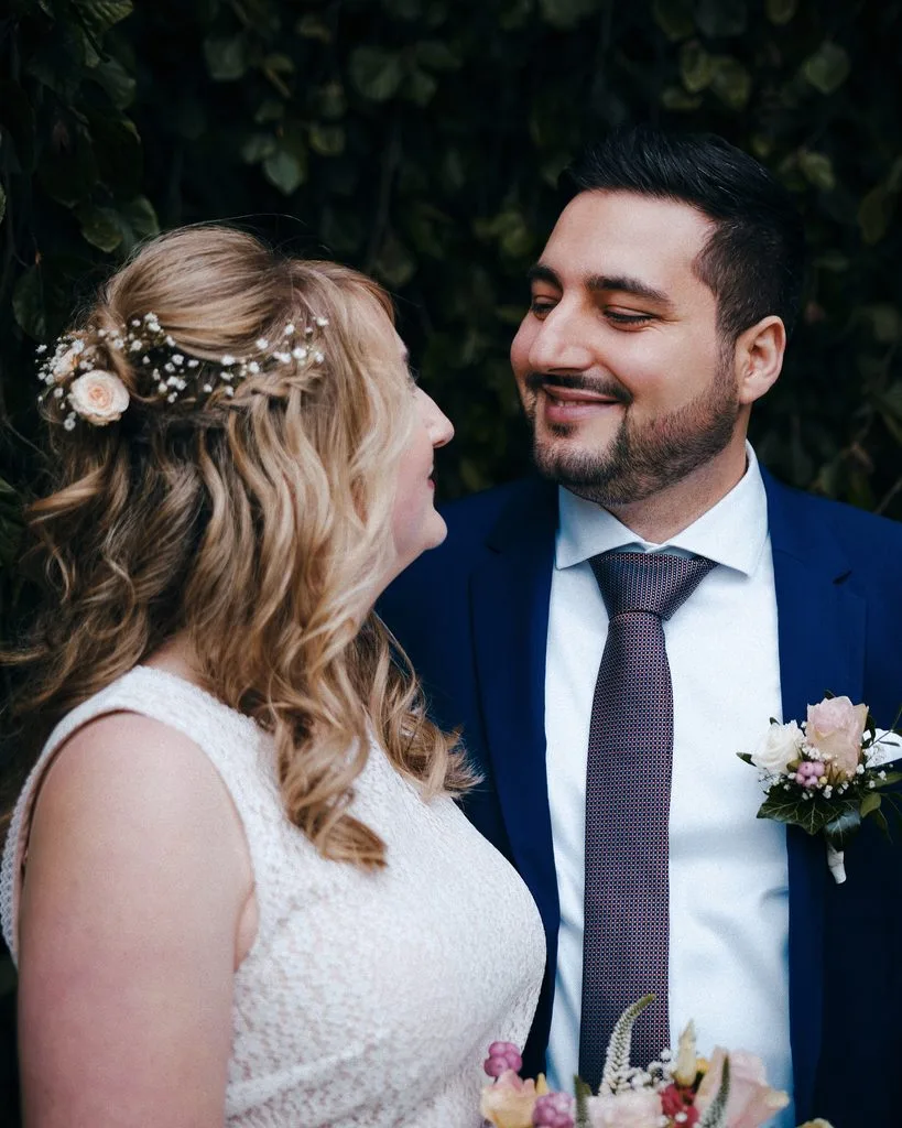 Bräutigam lächelt seine Braut mit Blumen im Haar an