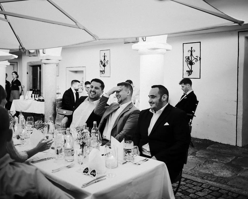 Hochzeitsgäste lachen an der festlichen Tafel im Innenhof, Schwarz-Weiß