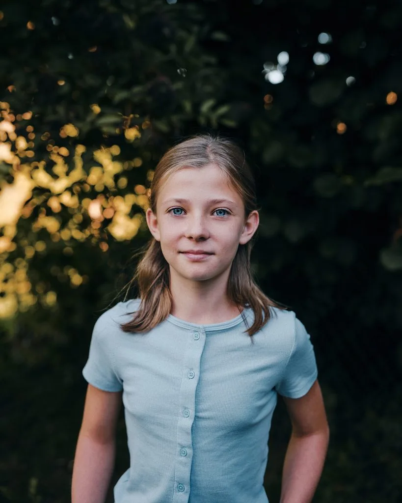 Portrait eines Mädchens im warmen Abendlicht vor grünem Laub