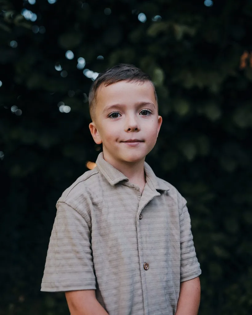 Portrait eines Jungen im Hemd vor dunklem Laub