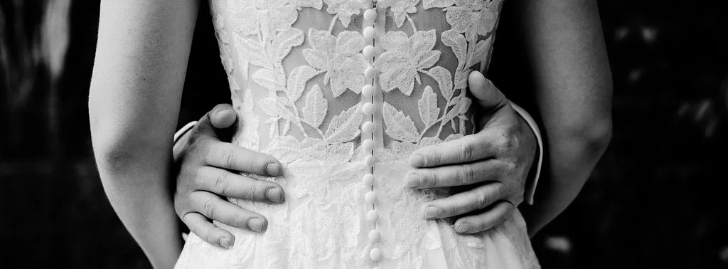 Bräutigam legt die Hände an die Taille der Braut, Rückenansicht des Spitzenbrautkleids mit Knopfleiste