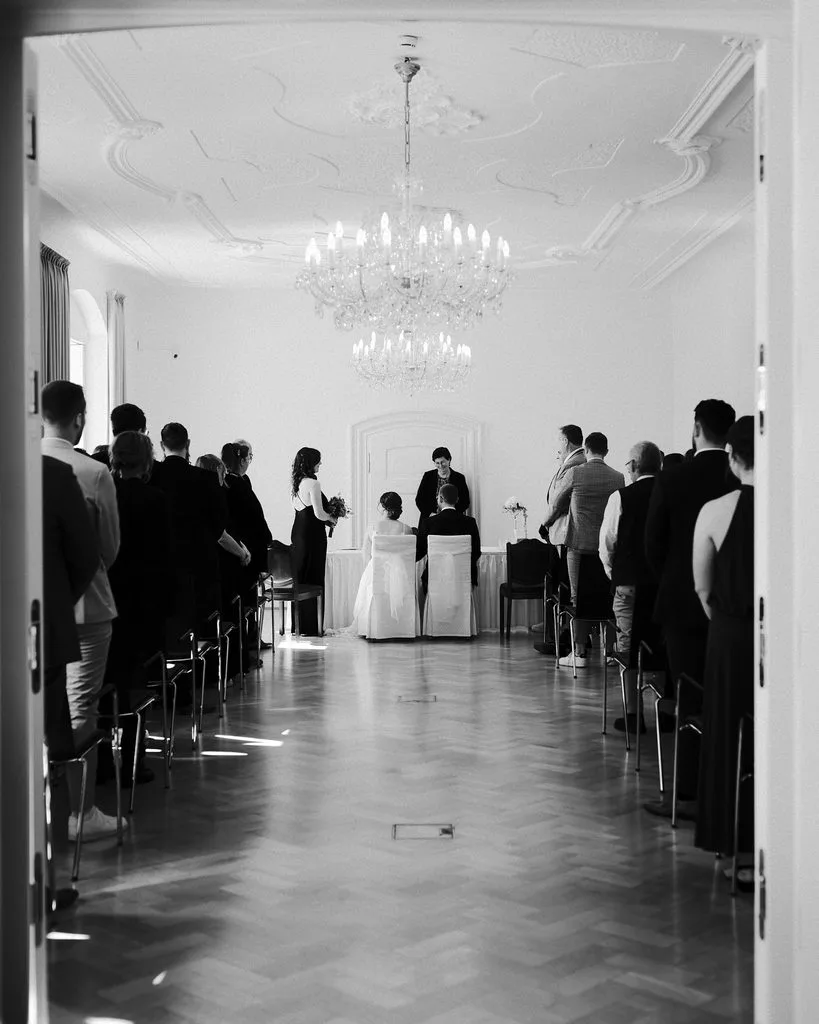 Standesamtliche Trauung im Saal mit Kronleuchter, Gäste stehen an den Seiten