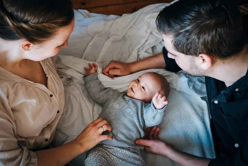 Eltern lächeln ihr Baby an, das zwischen ihnen auf einer Decke liegt