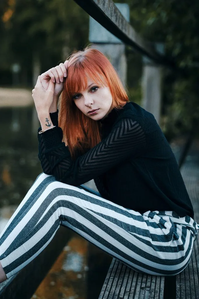 Frau mit roten Haaren und gestreifter Hose sitzt auf einem Steg – Portraitshooting