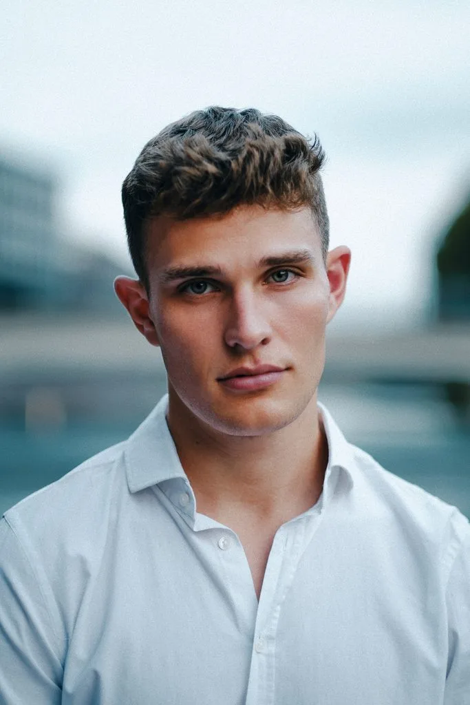 Portrait eines jungen Mannes im weißen Hemd vor unscharfer Stadtkulisse