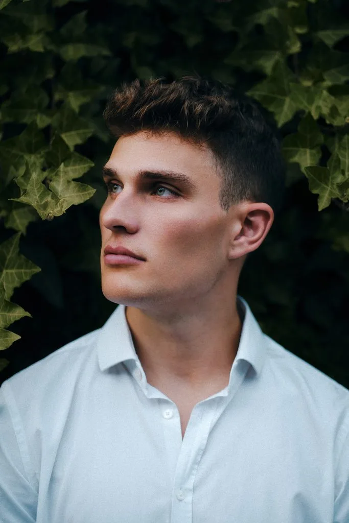 Portrait eines jungen Mannes im weißen Hemd vor Efeu
