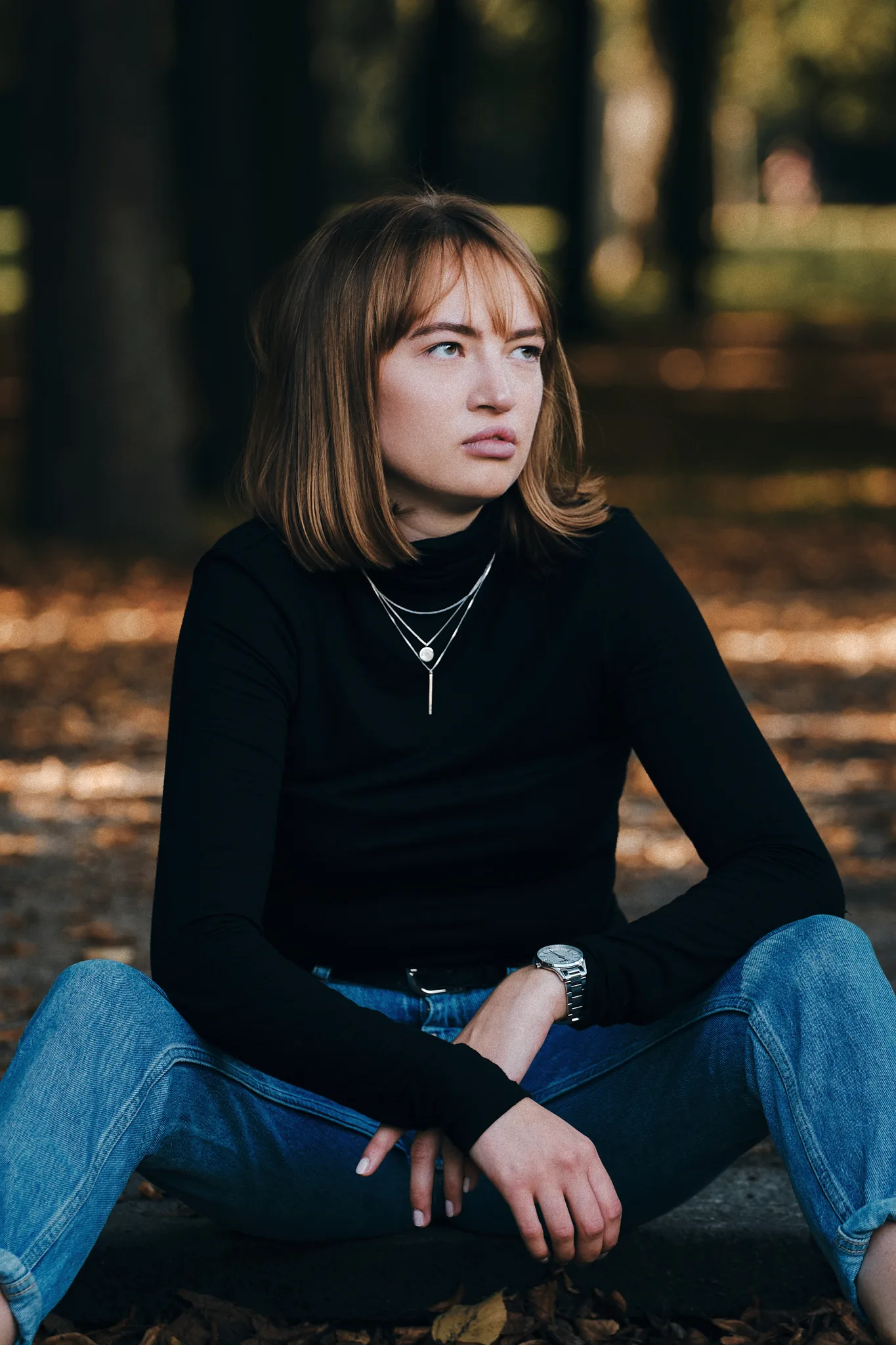 Junge Frau im schwarzen Pullover sitzt im Herbstlaub