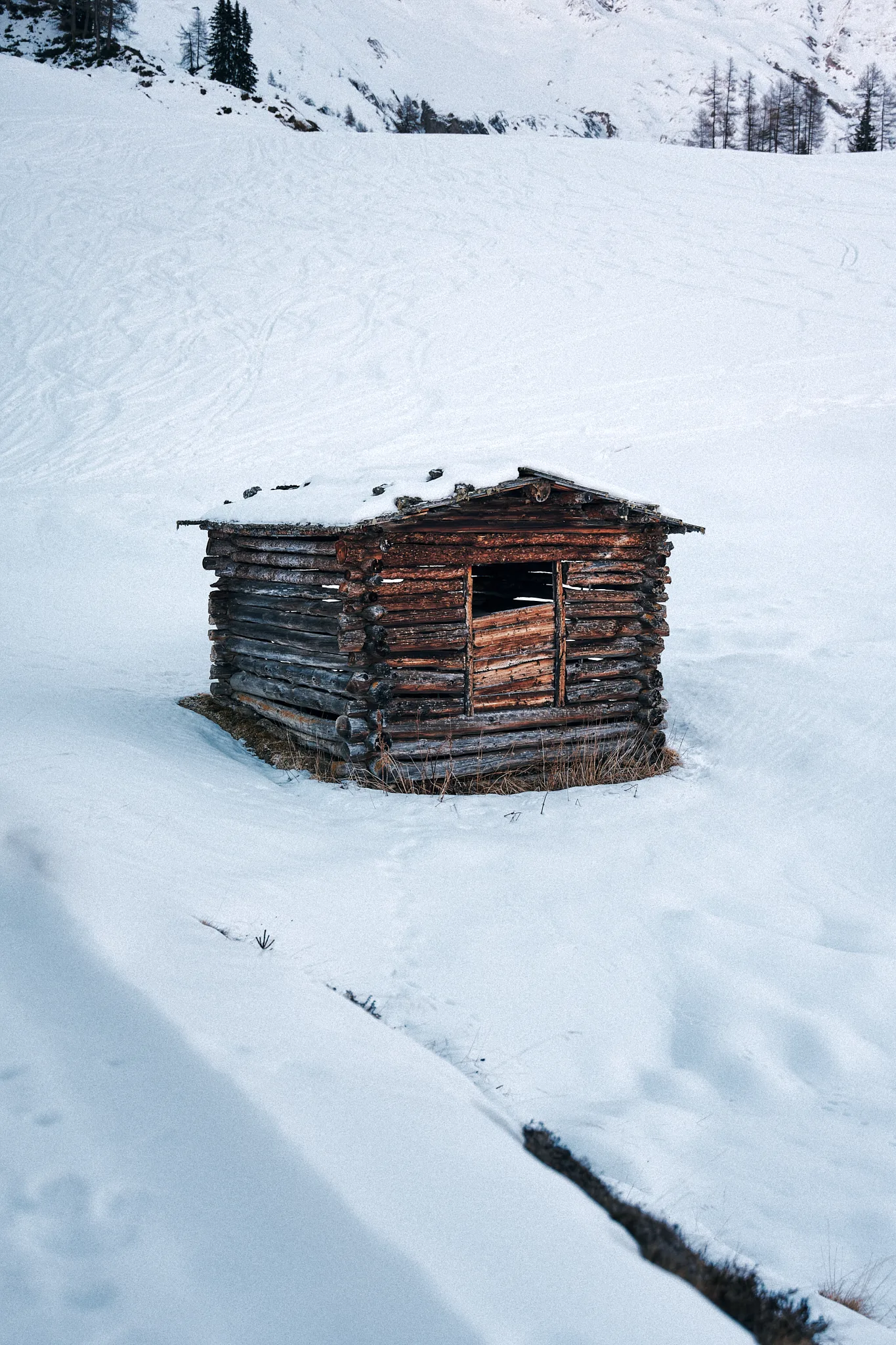 Verschneite Holzhütte an einem Berghang im Winter