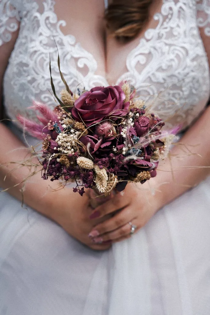 Braut hält einen Brautstrauß aus Trockenblumen vor ihrem Spitzenkleid