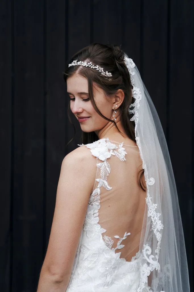 Braut mit Haarschmuck und Schleier blickt über die Schulter, rückenfreies Spitzenkleid